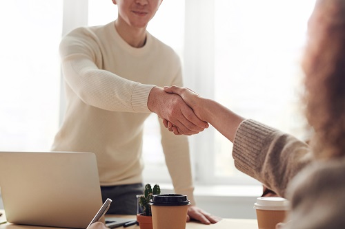 Two shake hands over a desk