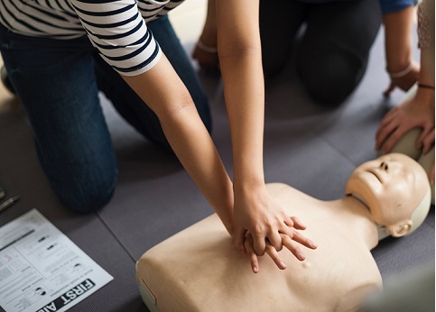 Three trainees gather around a dummy practicing CPR with first aid guidance card