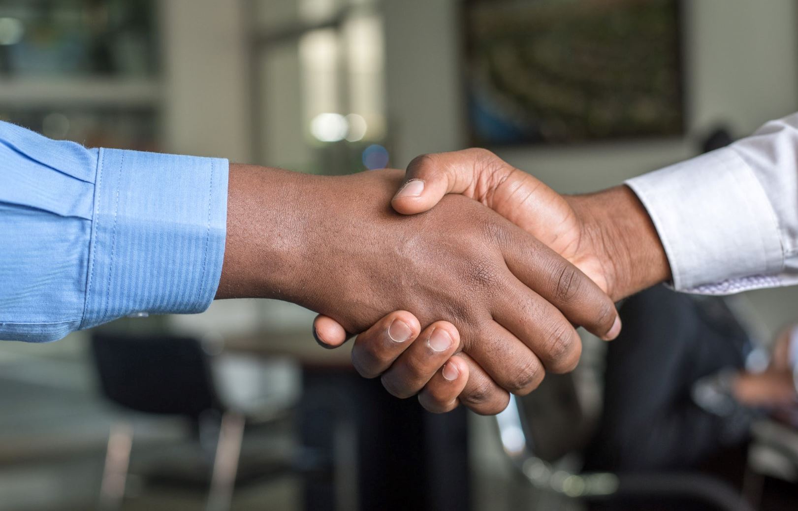 Two hands shake in front of an office background