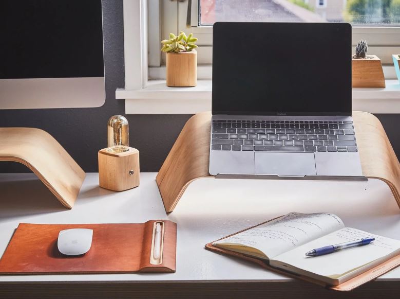 Home office desk with laptop on stand, open diary on desk and mouse on modern stylish mouse mat