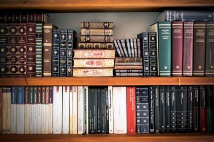 Two well stocked bookshelves, the lower containing same sized books and the upper an assortment of sizes