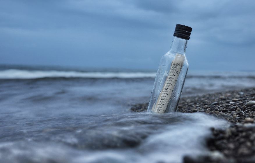 Message in a bottle washed up on shingle beach with a grey sky in the background