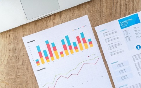 Report with bar and line chart  with a document placed on a wooden surface in front of a laptop