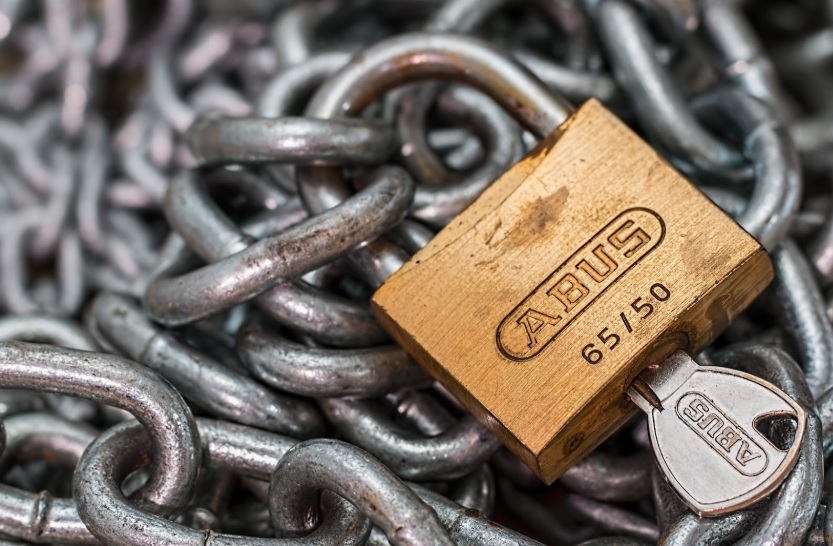 A brass padlock secures a coiled pile of steel chains