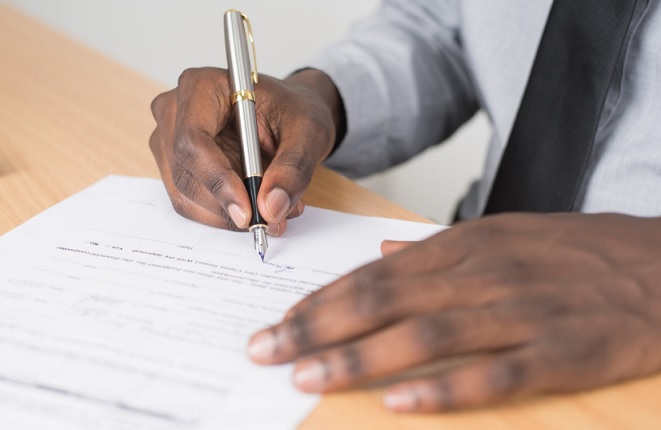 Employee with shirt and tie signs paperwork with a fountain pen at a wooden desk