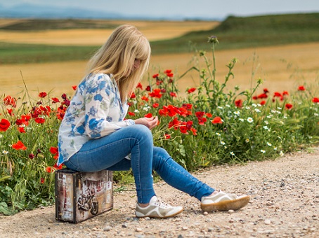 Women sitting on a suitcase along a gravel track bordered by Poppies with cornfields in the distance